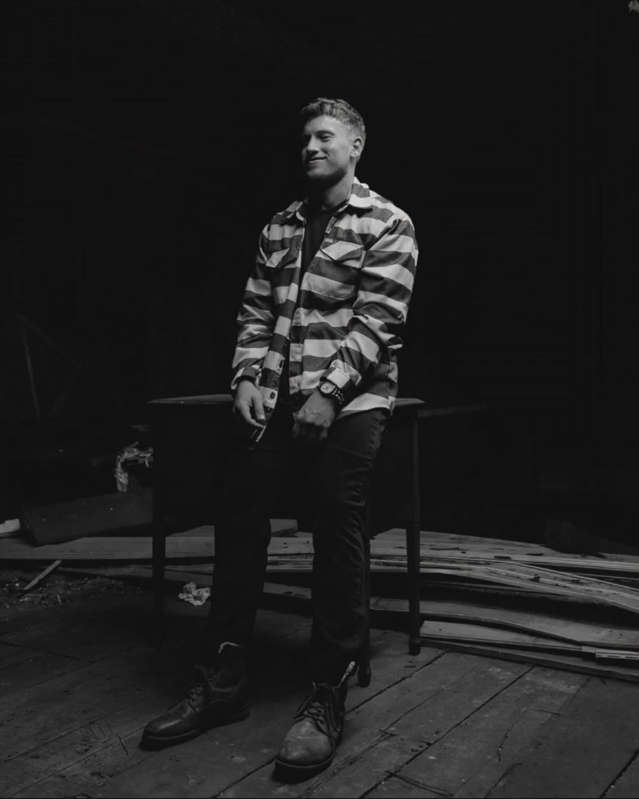 Ryan Zakrzewski, founder of Positive Empathetic's, leaning against a work table in a stripped-out attic, looking off to one side.
